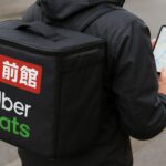 出前館とUber Eatsの配達バッグとスマホで地図アプリを表示する配達員の手元