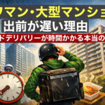 タワマン・大型マンションの前で、配達員がヘルメットをかぶり困った表情で立っている。背景に高層マンションが並び、時計のイラストが時間の遅れを示す。手前には配達用の食事ボックスが置かれている。
